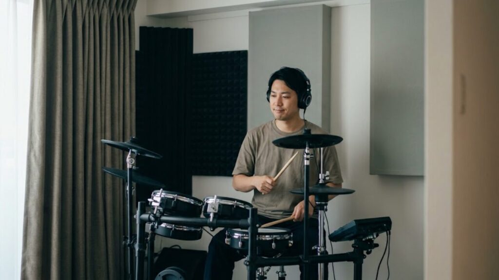 自宅マンションの自室で、電子ドラムをヘッドホンをして静かに、かつ集中して練習する日本人男性ドラマーの様子。防音対策が施された環境で、安心してドラムを楽しむ姿。
