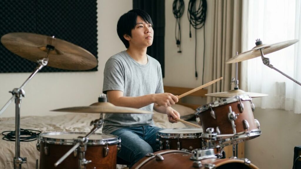ドラムセットの前で少し苦悩する日本の初心者ドラマー。なぜ難しいと感じるのか、その心理的な壁を象徴する。